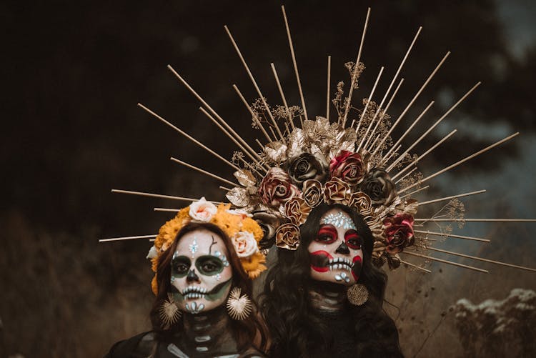 Portrait Of Two Young Women Wearing Sugar Skull Makeup And Flower Crowns As The Sign Of A Mexican Tradition