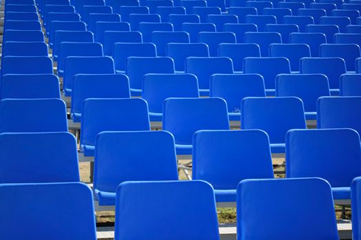 Rows of empty blue stadium seats arranged in an outdoor setting.