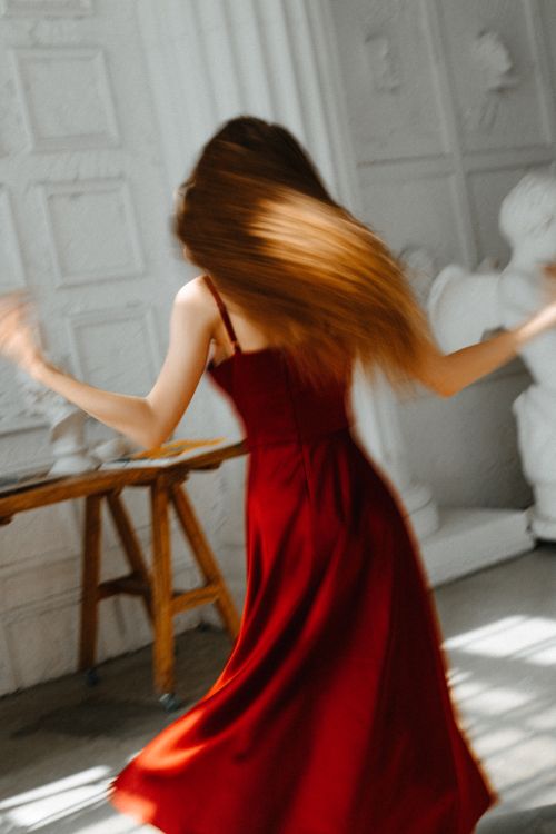 Free A woman in a red dress gracefully dances in a bright, art-filled room. Stock Photo