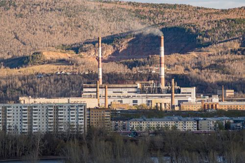 Free A power plant with smokestacks emitting smoke, surrounded by buildings and forest. Stock Photo