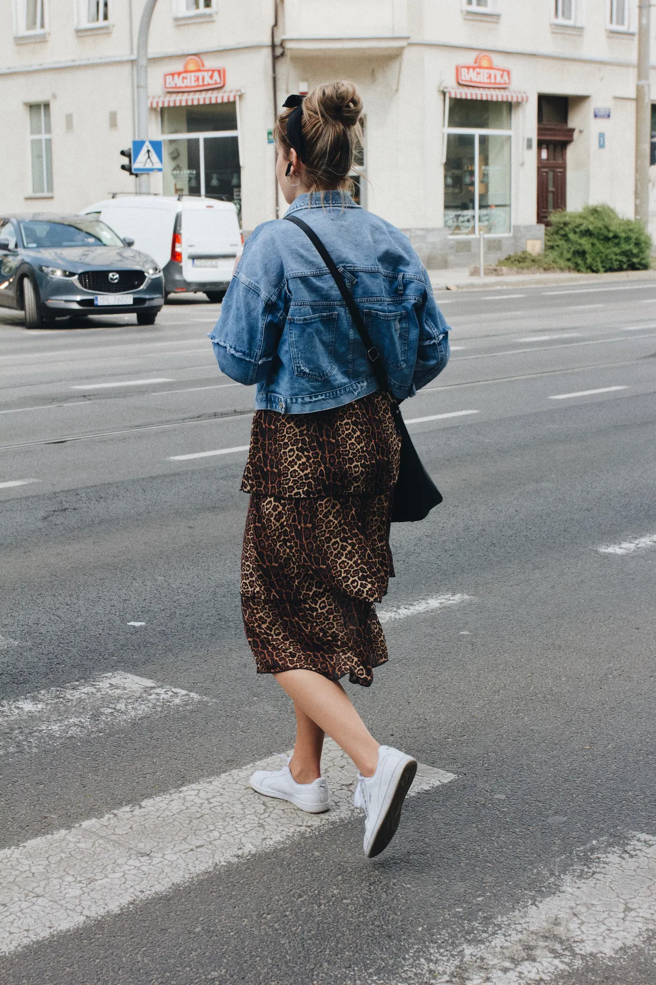 denim-jacket-midi-skirt-airport Woman in a denim jacket with a leopard midi skirt and white sneakers crossing the street