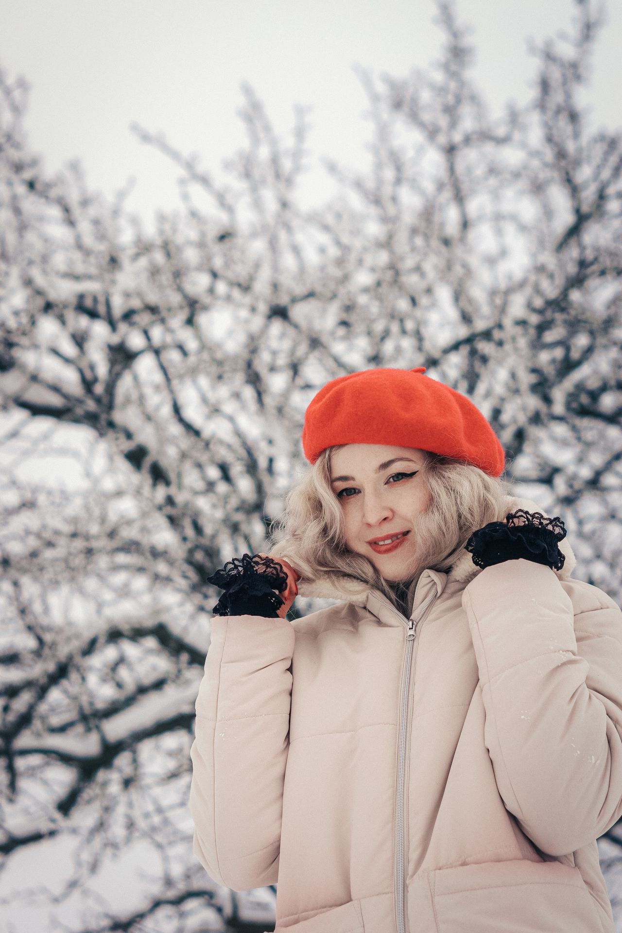 Smiling woman in a red beret and winter coat on a snowy day
