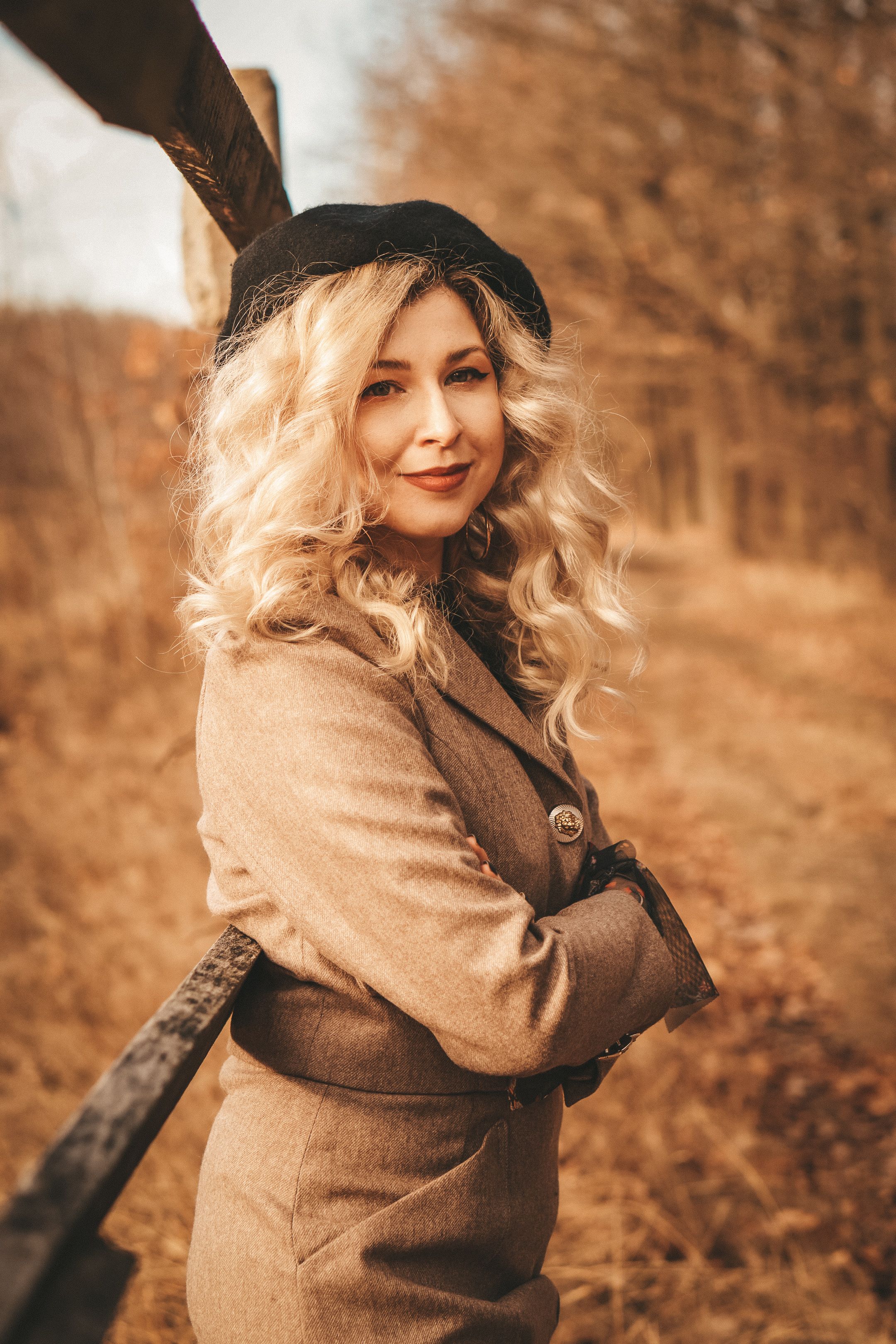 Elegant autumn portrait of a smiling woman with wavy blonde hair and fashionable attire.
