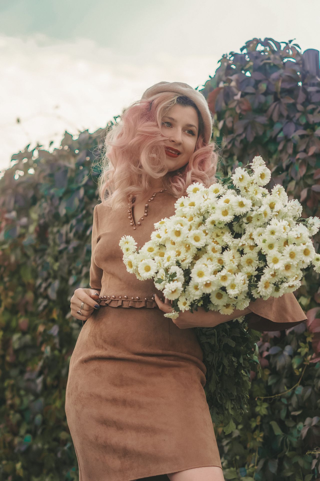 Woman in a tan suede-look dress holding a bouquet of white flowers