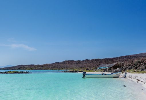 Explore a tranquil tropical beach with turquoise waters, a boat, and a distant island view.