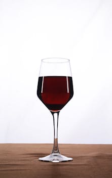 A tall wine glass filled with red wine against a white background on a brown surface.