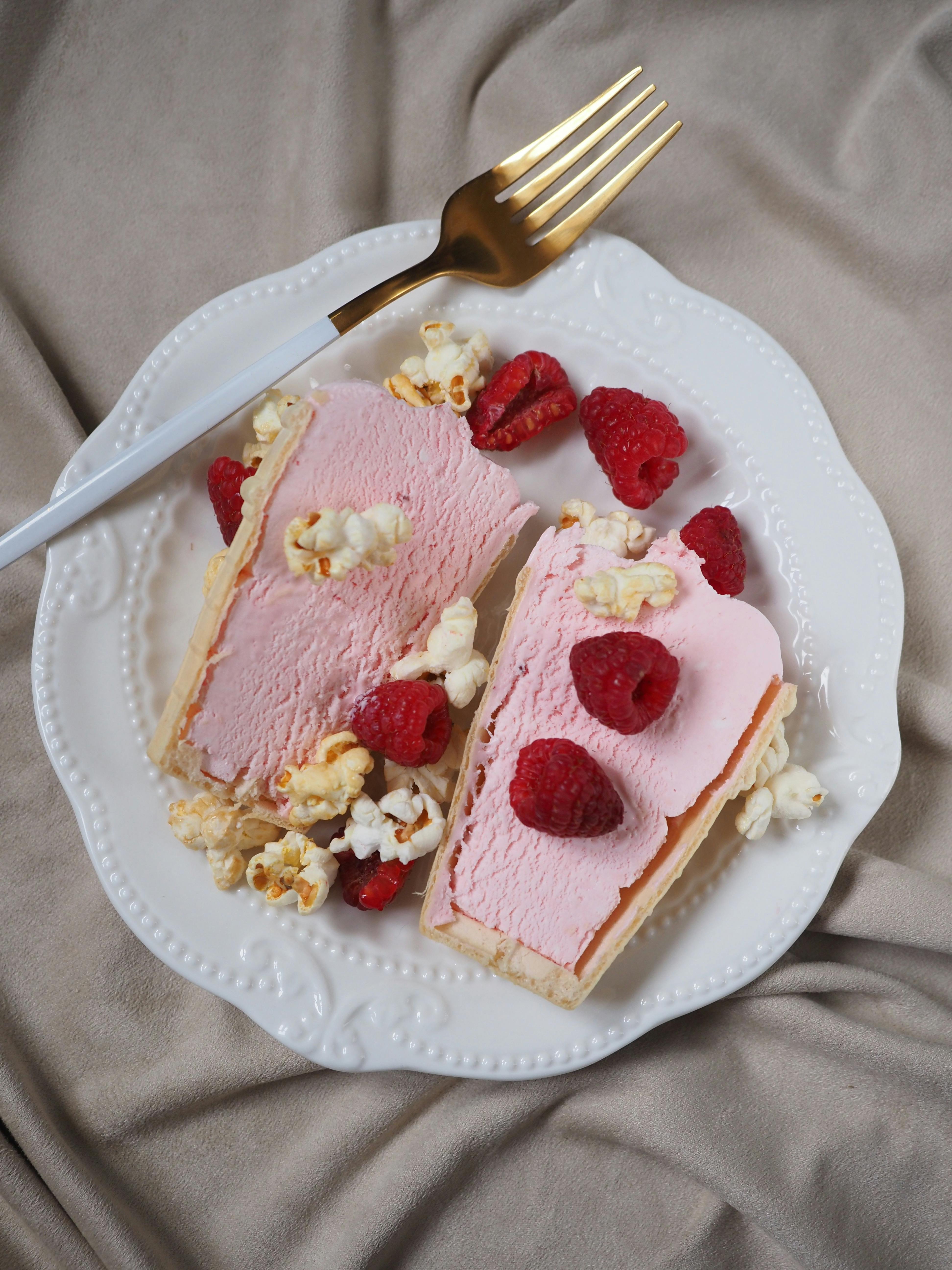 Delicious raspberry ice cream cake on a plate, garnished with fresh raspberries and popcorn.