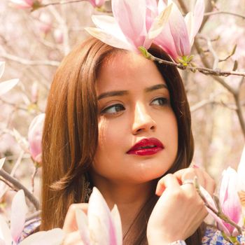 Portrait of a woman with red lips among blooming magnolia flowers, exuding elegance.