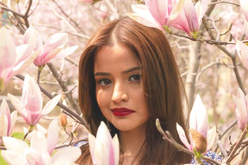 Free Close-up of a woman with red lips surrounded by pink blossoms during spring. Stock Photo