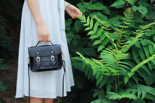 Free Close-up of a woman holding a black handbag, wearing a striped dress, beside lush green plants. Stock Photo