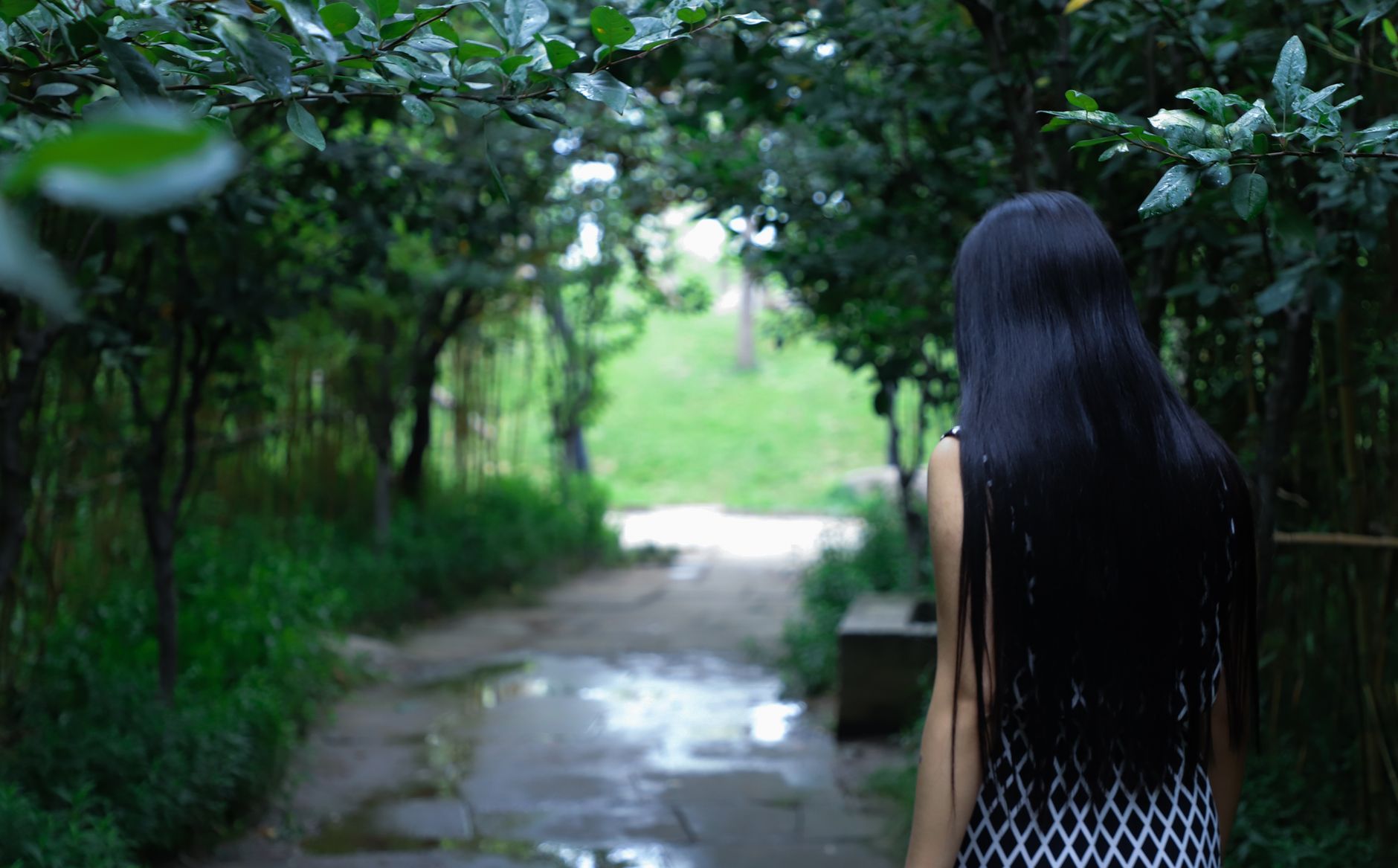 A woman walking through a lush green pathway surrounded by trees