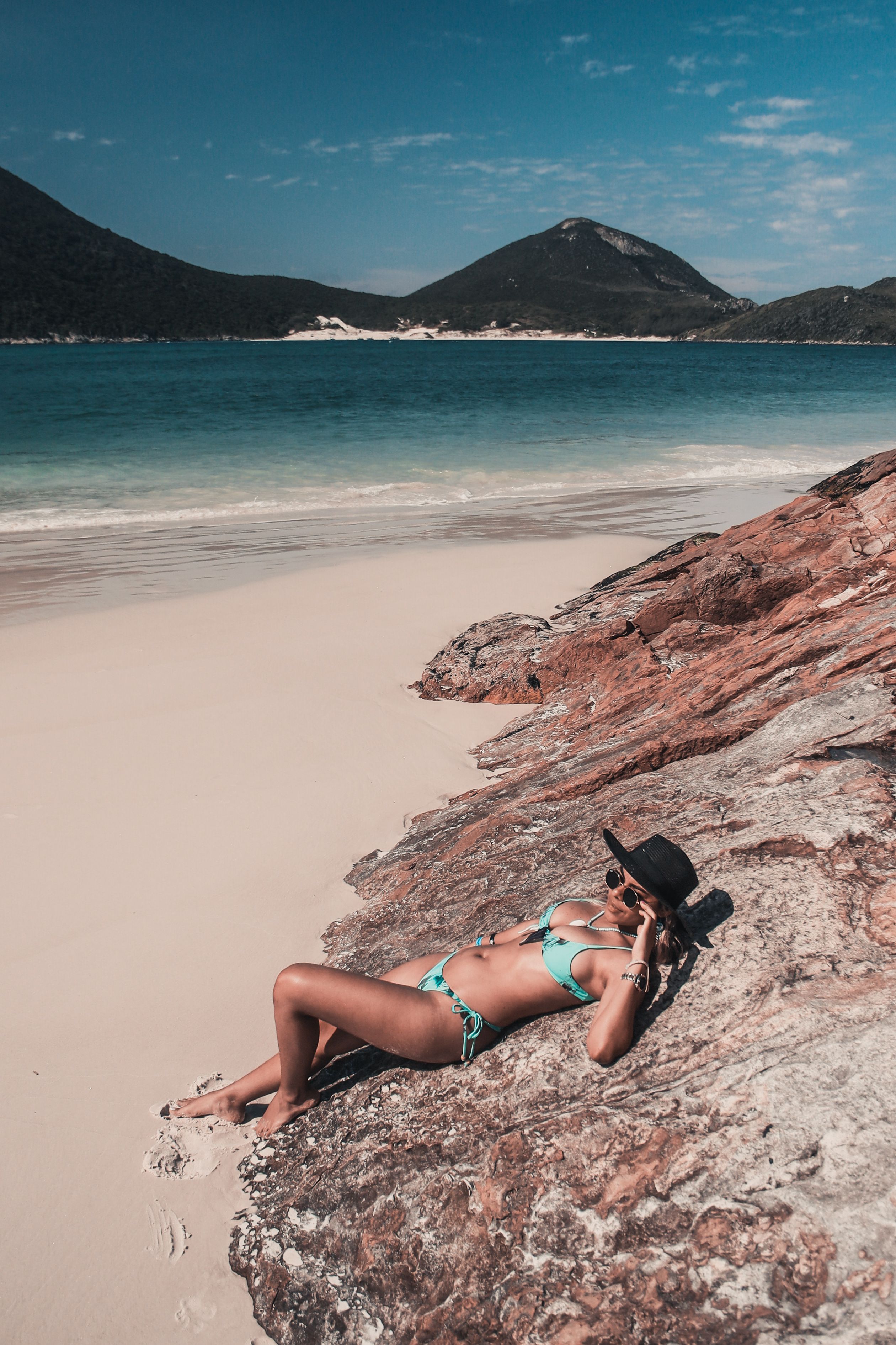 Uma mulher tomando sol em uma linda praia com céu azul claro e águas turquesa.