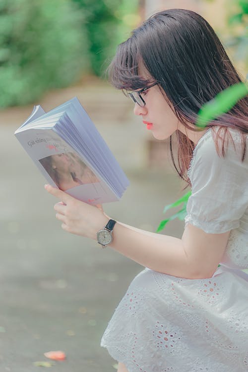 Free Woman Sitting While Reading Book Outdoors Stock Photo