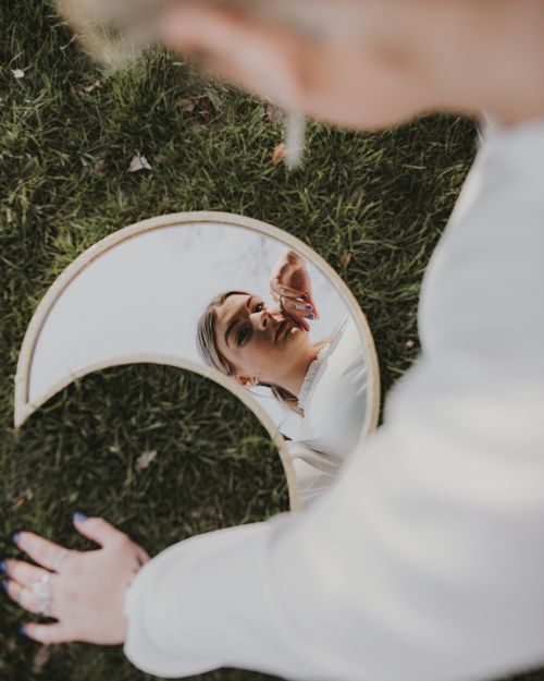 Free Artistic portrait reflection of a woman in a crescent mirror placed on grass. Stock Photo