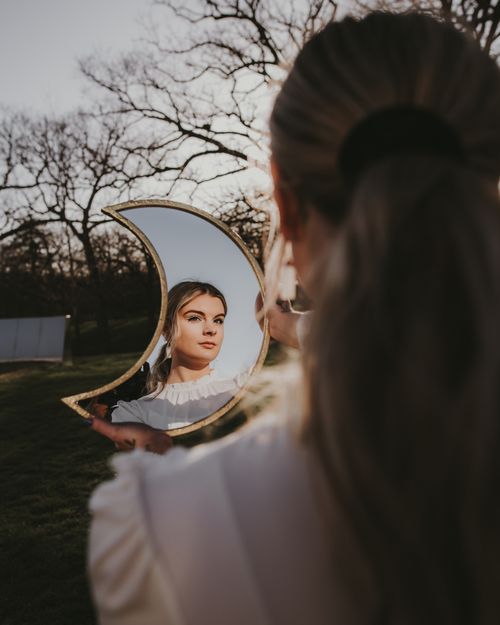 Free A woman holds a crescent moon mirror, reflecting her face in an outdoor setting. Stock Photo