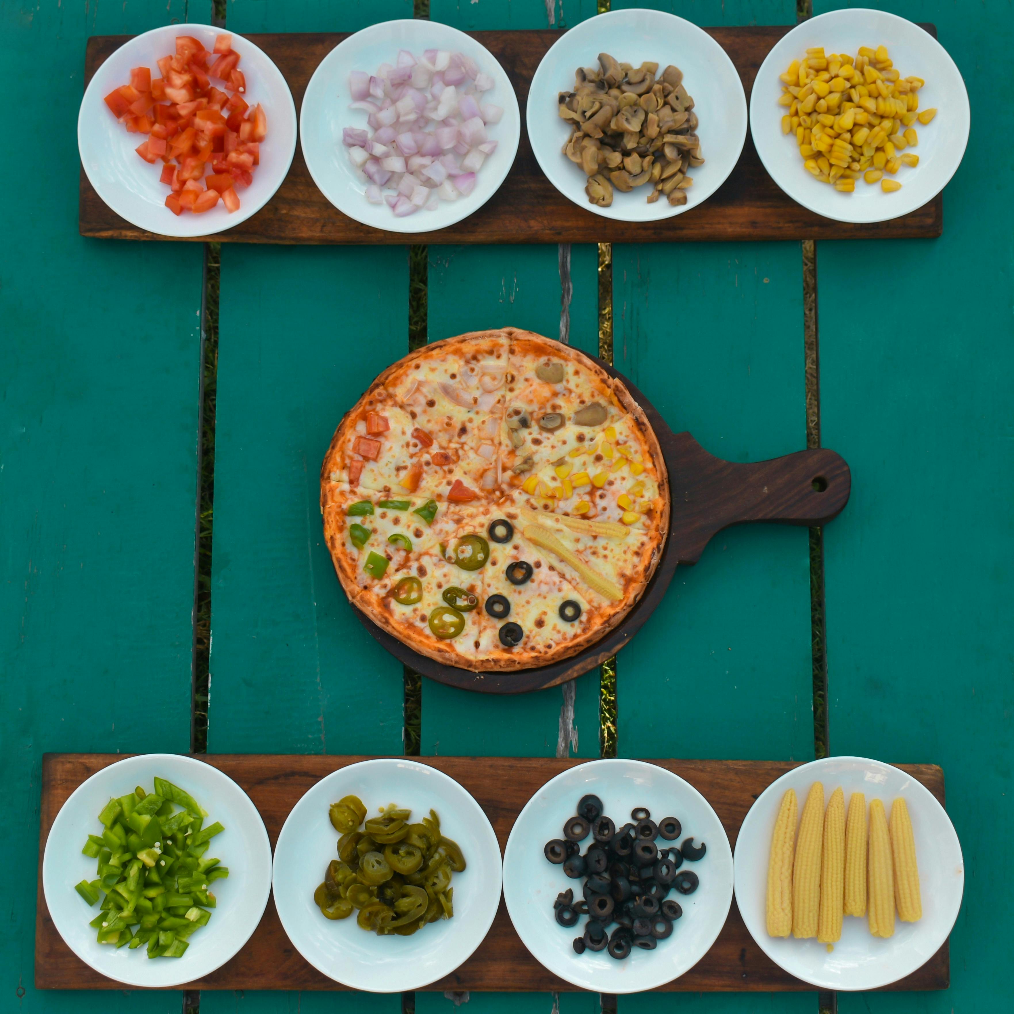 Top view of vegetarian pizza surrounded by fresh ingredients artistically arranged on plates.