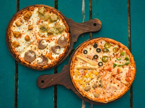 Free Two pizzas with various toppings on wooden boards over a rustic green table, captured in a top-down view. Stock Photo
