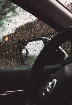View from inside a car during rain, showcasing droplets on the window and the steering wheel.