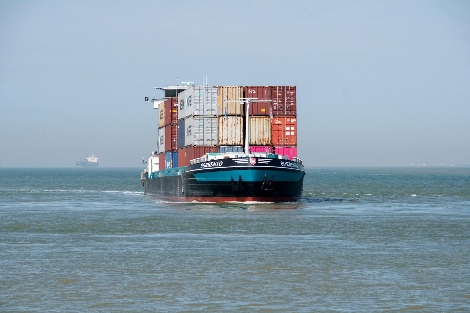 Front view of a large cargo ship loaded with colorful containers in open ocean.