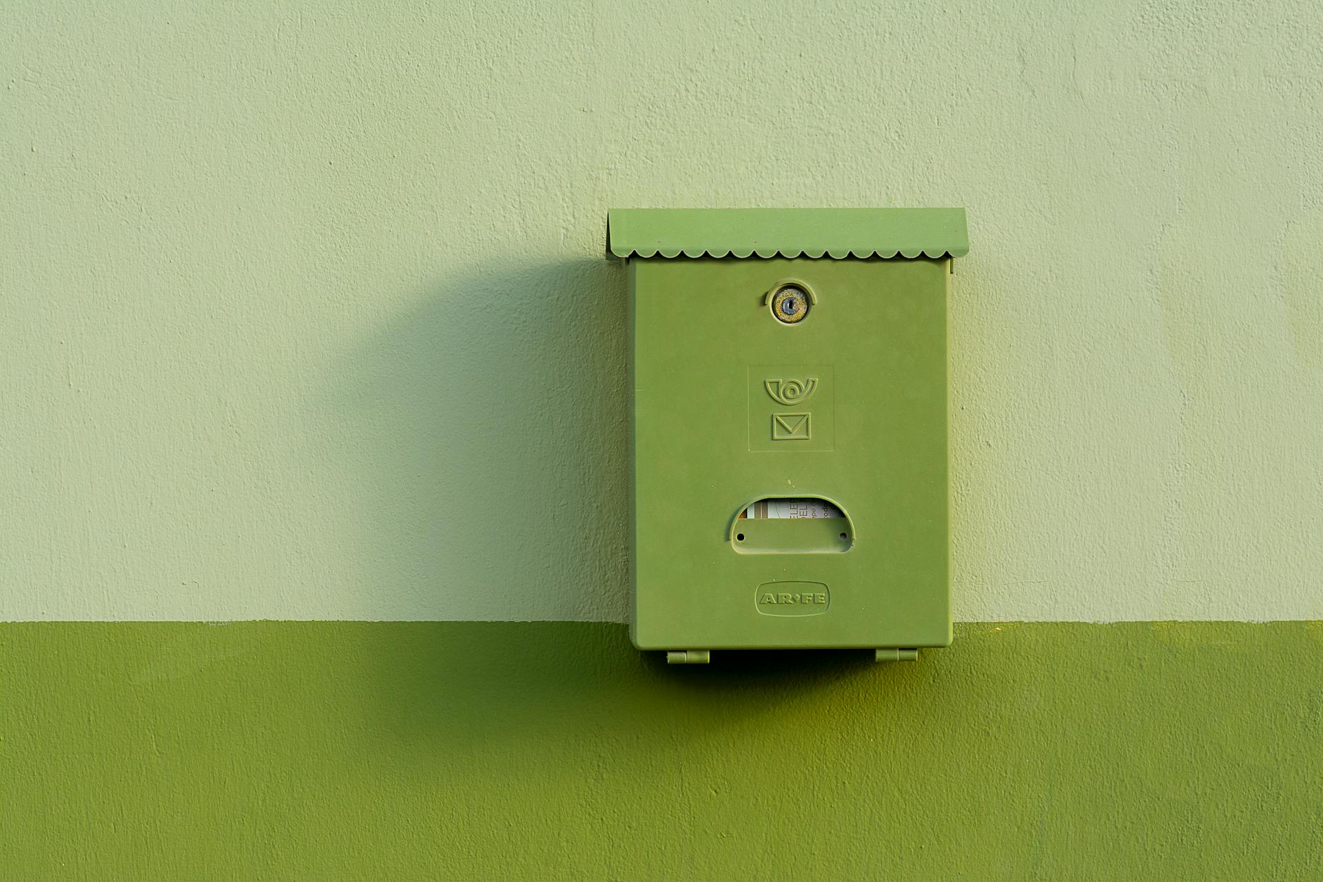 A simple green mailbox mounted on a two-tone green building facade, offering contrast and minimalism.