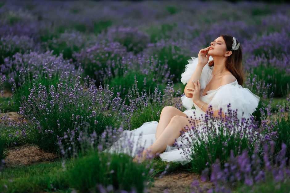 A serene woman in a white dress seated in a vibrant lavender field, embracing the fragrance.