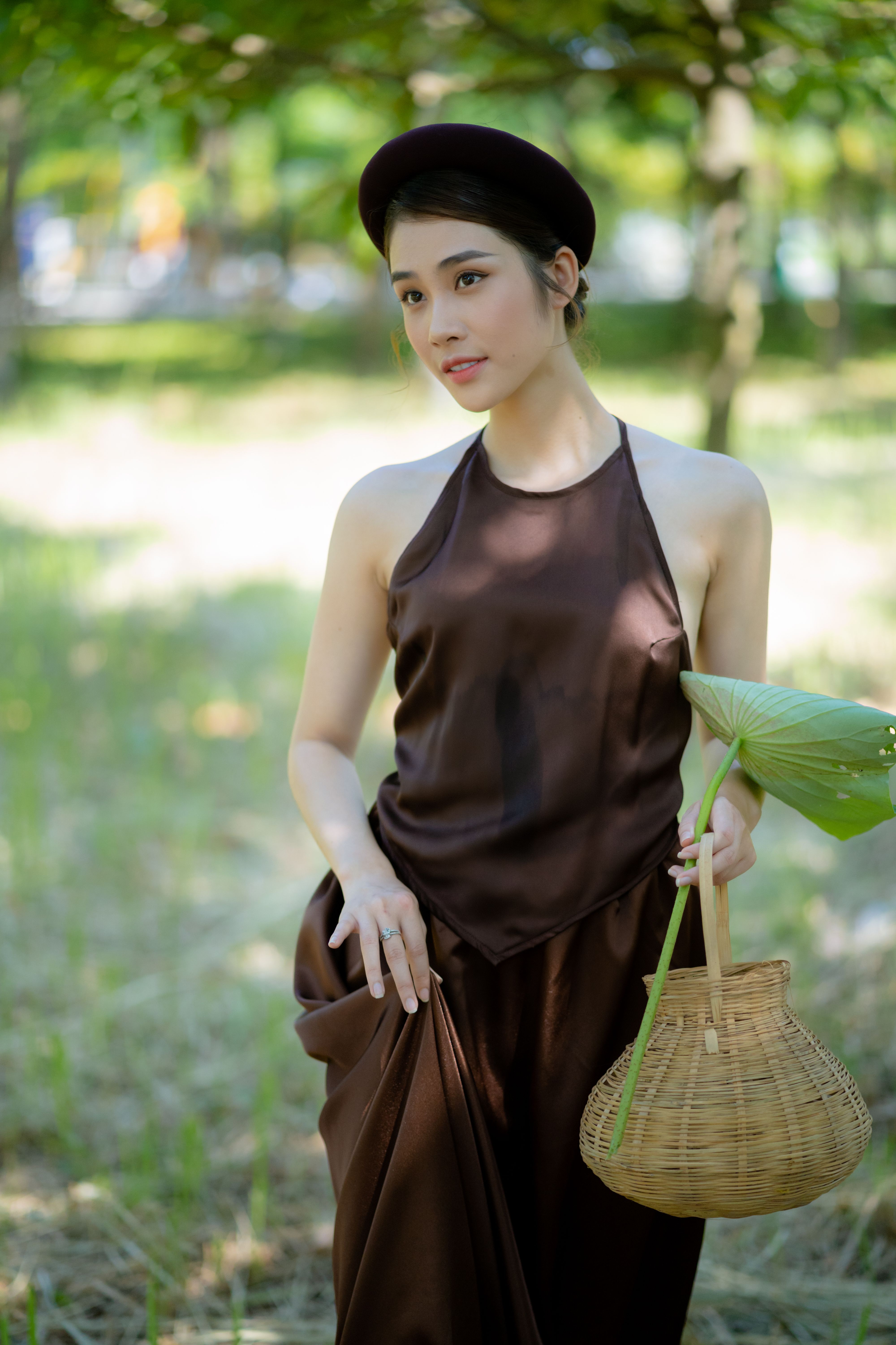Beautiful woman in brown attire holding a basket in a serene outdoor setting.