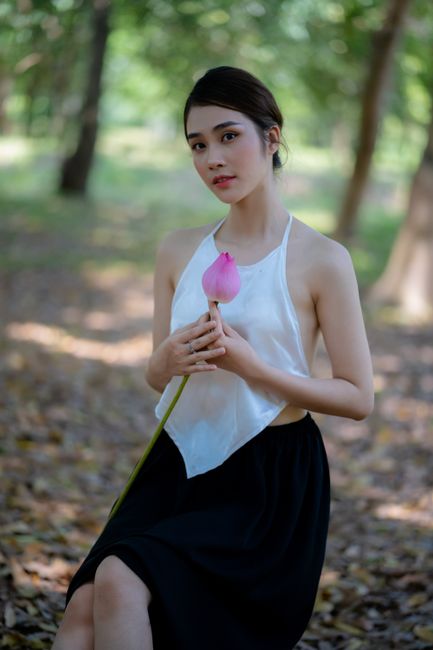 A serene portrait of a woman holding a lotus flower in a sunlit forest, emphasizing natural beauty and tranquility.