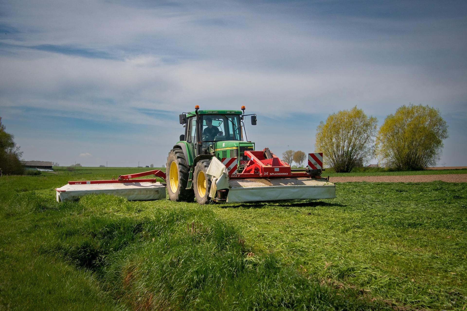 A green tractor mows a grass field on a sunny day, showcasing modern farming equipment.