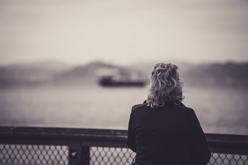 Free Grayscale Photo of Woman Standing Near Metal Fence Stock Photo