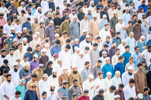 Free A large gathering of people praying outdoors in traditional Muslim attire, illustrating religious devotion and unity. Stock Photo