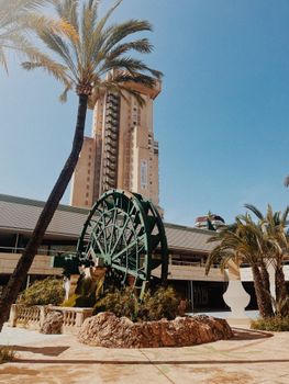 Scenic view of Benidorm with a palm-lined urban landscape and a prominent wheel sculpture.