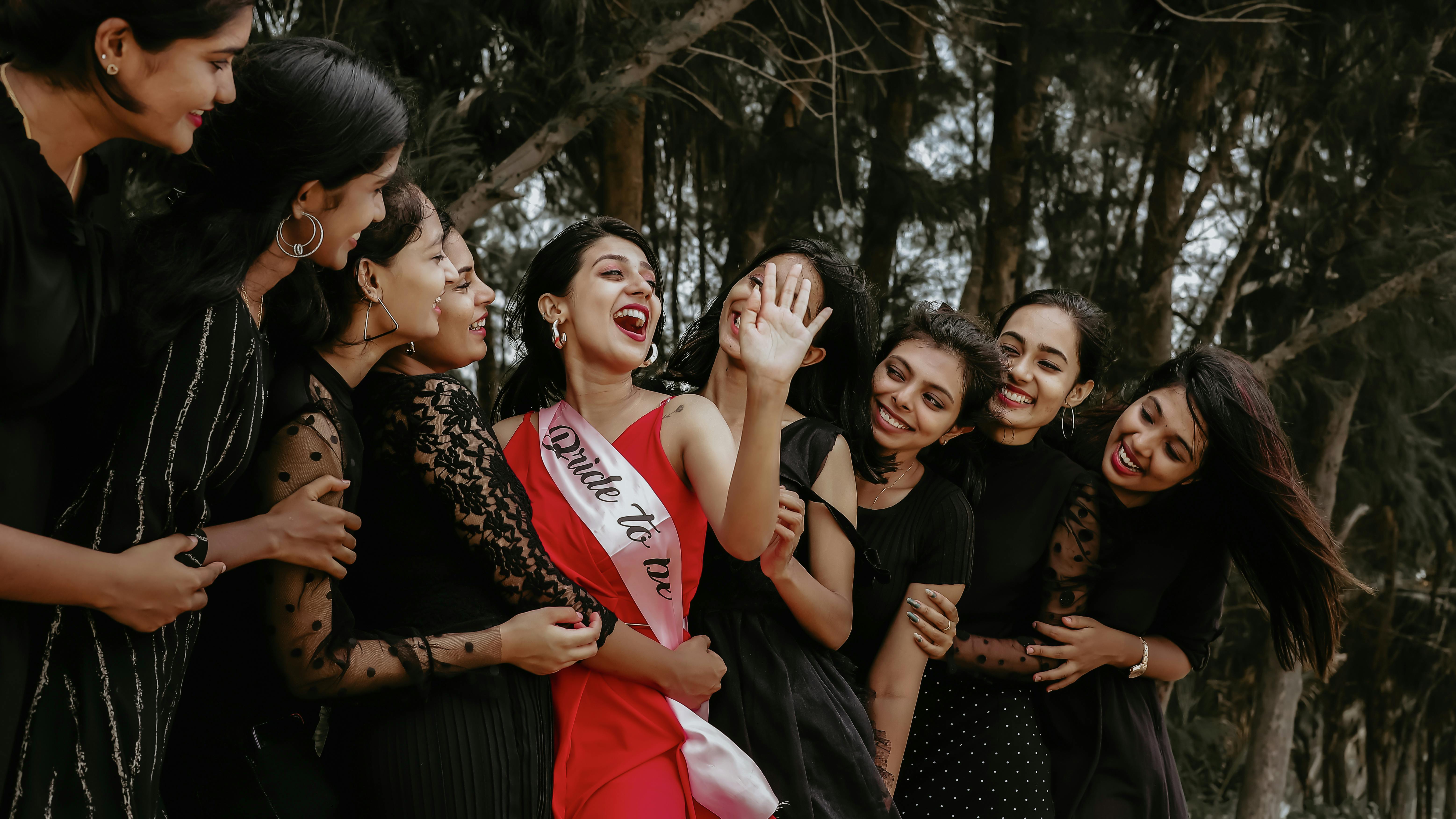 A group of women joyously celebrating outdoors with the bride-to-be wearing a sash.