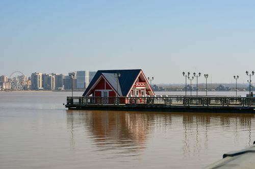 Free Charming red house on a pier with a city skyline backdrop across a tranquil water body. Stock Photo
