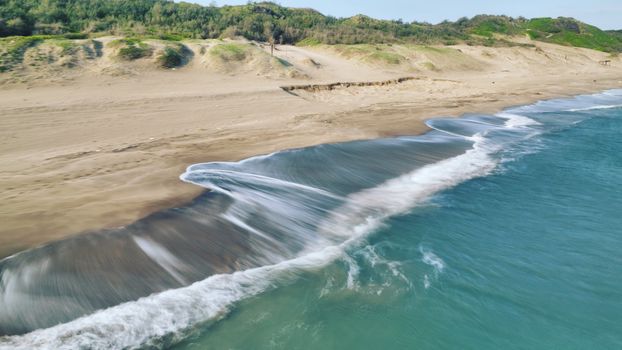 Aerial view of a tranquil coastal landscape with gentle waves and sandy beach.