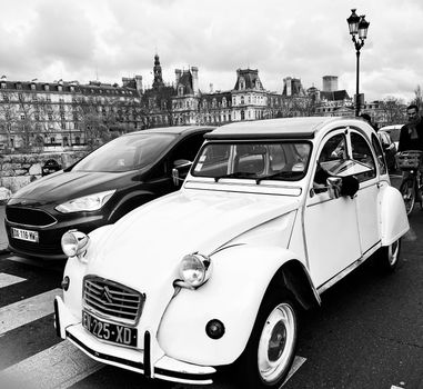 Classic Citroën 2CV car parked on a Paris street with historic architecture in black and white.