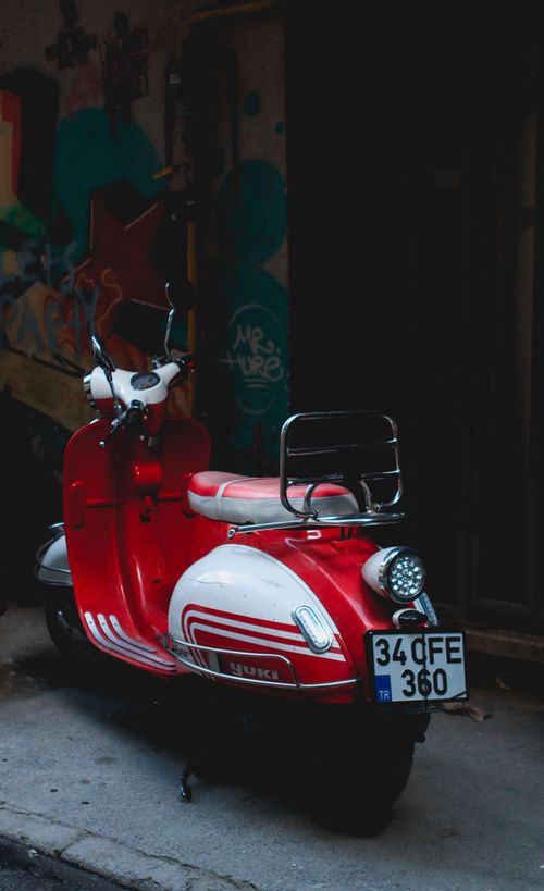 Free Red vintage scooter parked by a colorful graffiti wall, creating an urban contrast. Stock Photo