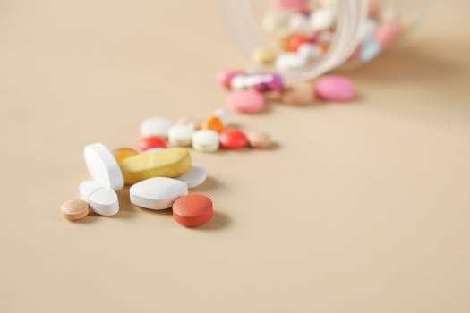 Close-up of various pills spilling from a container on a beige surface.
