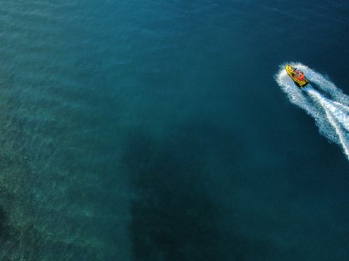 Free Aerial photo of a speedboat creating white wake on the blue ocean, captured with a drone. Stock Photo