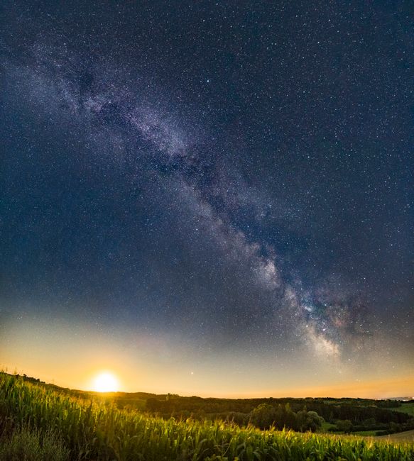 Captivating view of the Milky Way galaxy with a sunset over a serene green field.