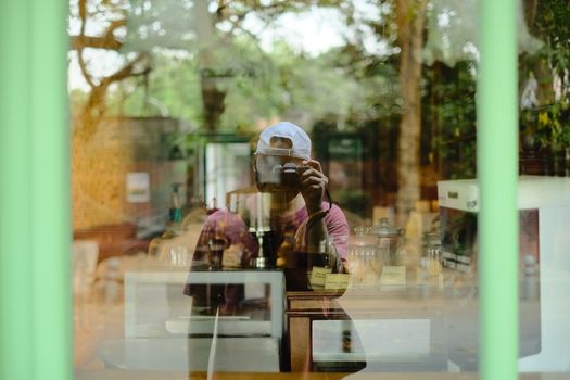 A photographer captures his reflection in a glass window, blending indoors and outdoor elements.