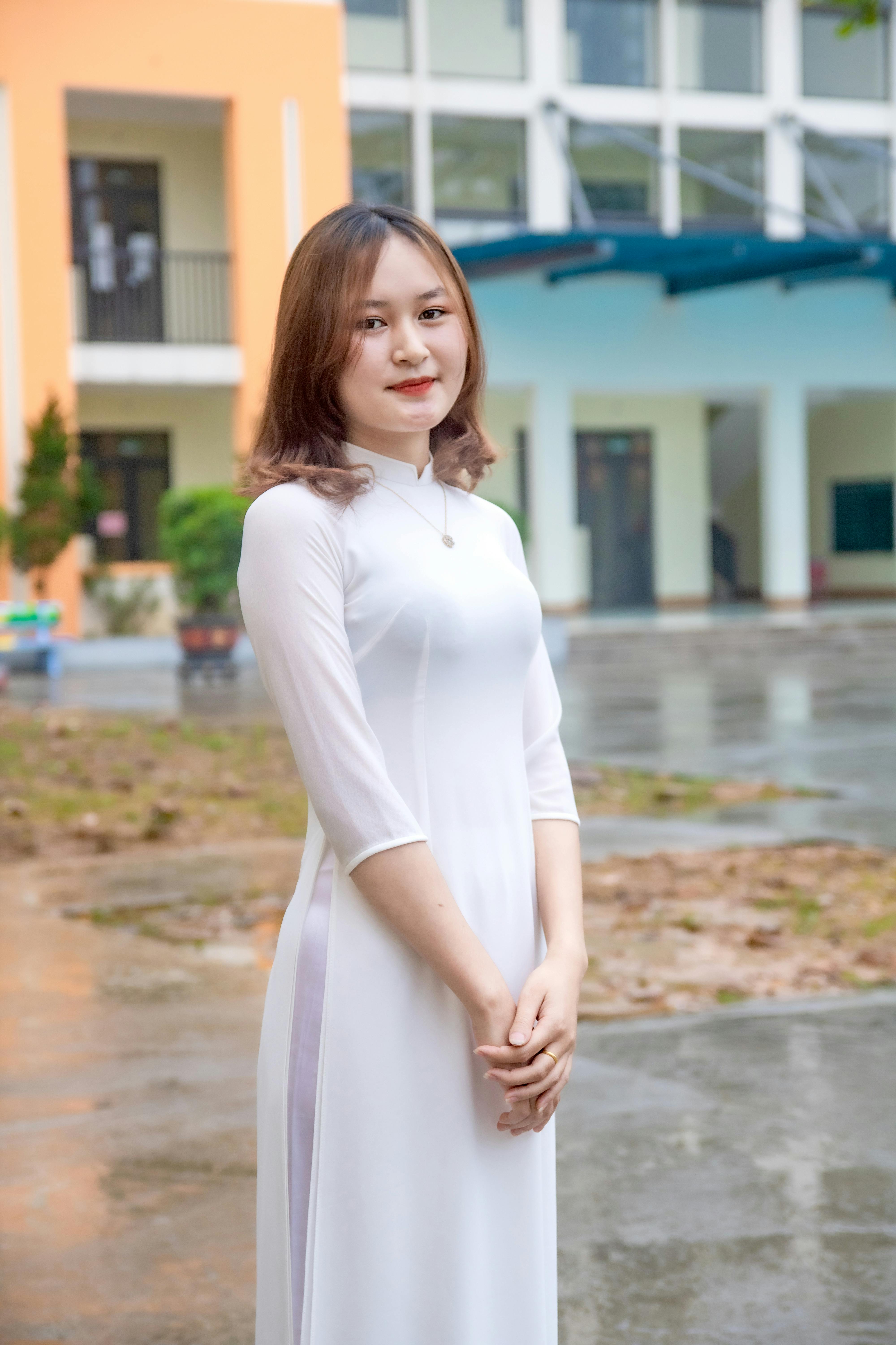 Elegant young woman in white dress posing outdoors with architectural backdrop, showcasing fashion style.