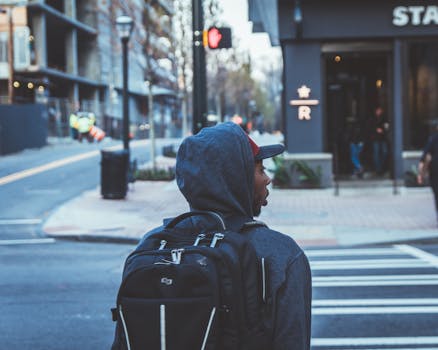 African American man with backpack crossing a city street on a cool day.