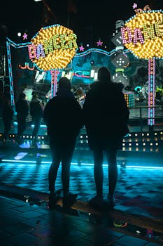 Silhouettes at an illuminated carnival ride, capturing a vibrant night scene.