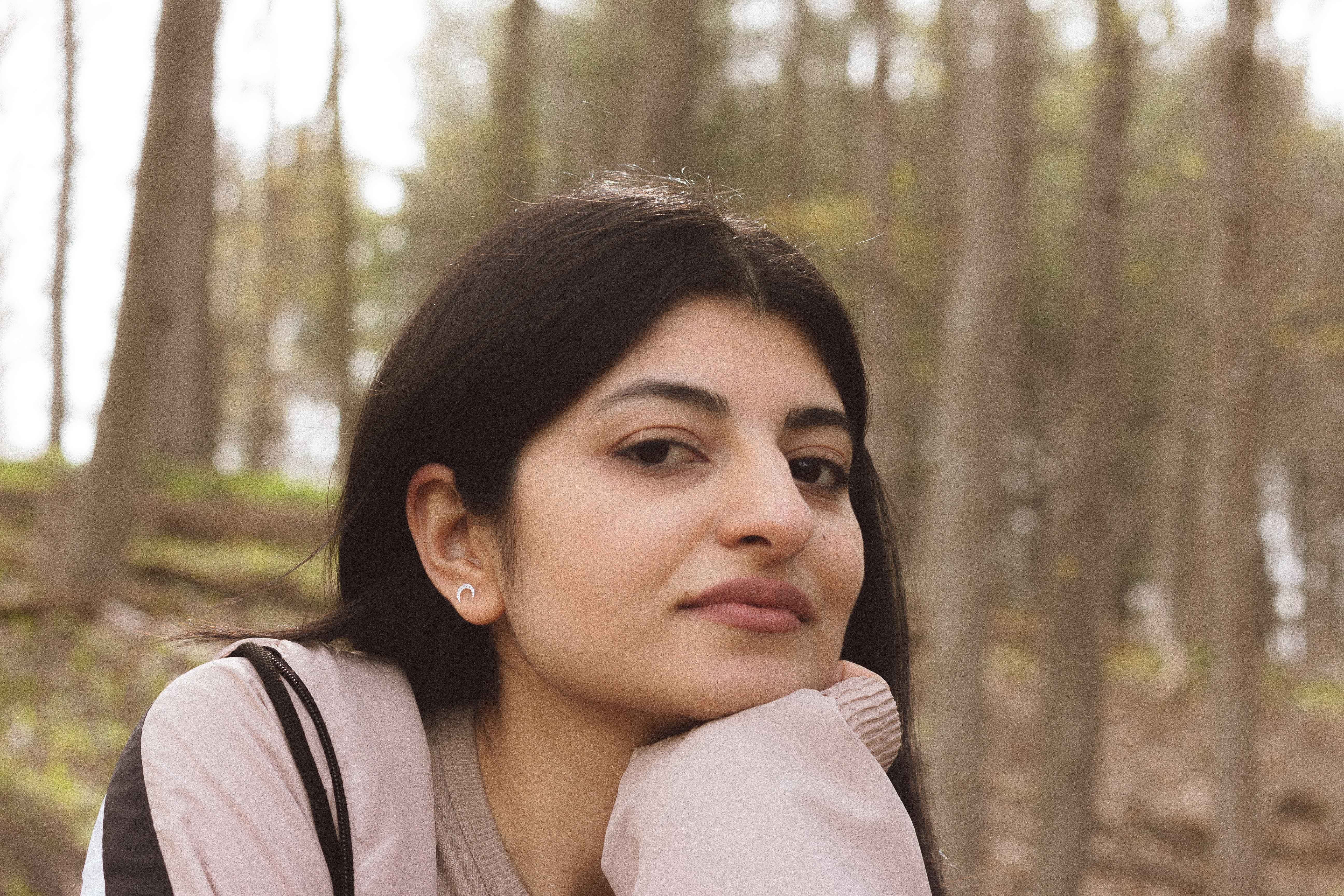 A serene portrait of a woman resting her chin on her hand in a tranquil forest setting.