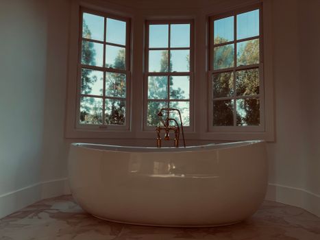 Luxurious freestanding bathtub with large windows, offering a serene view of greenery.