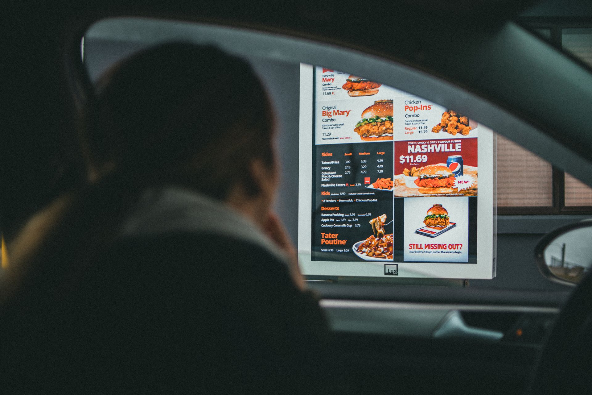 A woman in a car views the menu at a fast food drive-thru, ready to order her meal.