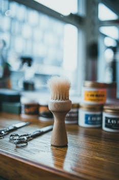 Close-up of a barber's brush with jars and scissors on a wooden table in a rustic barbershop setting.