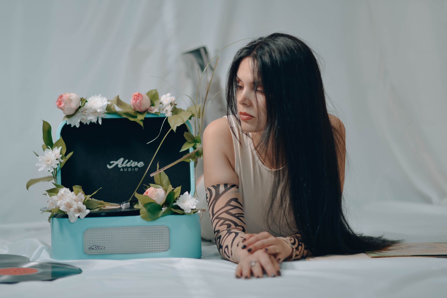 Young woman with long dark hair relaxing by a floral vinyl player, enjoying serene ambiance.