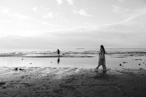 Free A black and white photograph of a woman walking along the beach shoreline, creating a calm and serene atmosphere. Stock Photo