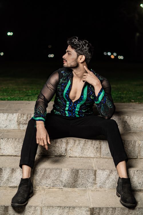Free Stylish man in patterned shirt sits on steps, posing confidently at night. Stock Photo